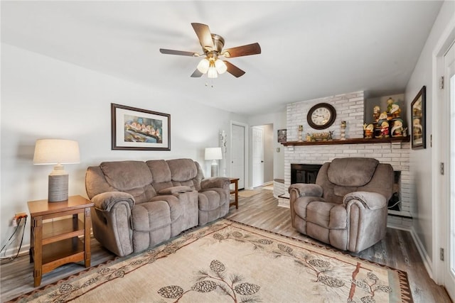 living room with a ceiling fan, a brick fireplace, light wood-style flooring, and baseboards