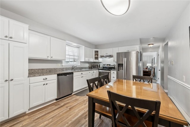 kitchen with glass insert cabinets, dark stone countertops, stainless steel appliances, under cabinet range hood, and white cabinetry