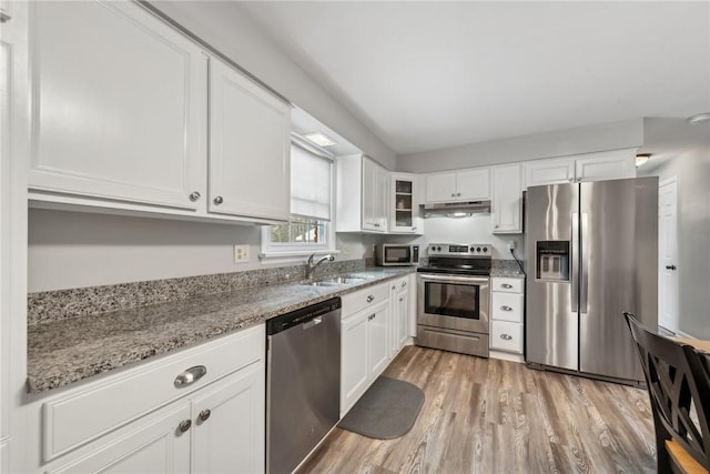 kitchen featuring white cabinets, light stone countertops, stainless steel appliances, under cabinet range hood, and a sink