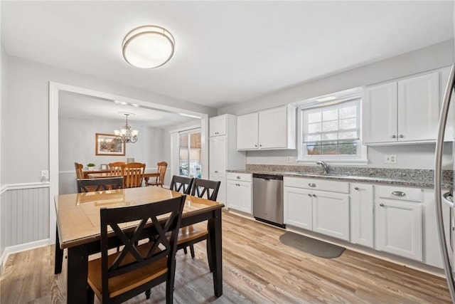 kitchen featuring white cabinets, light wood-style flooring, hanging light fixtures, light stone countertops, and stainless steel appliances