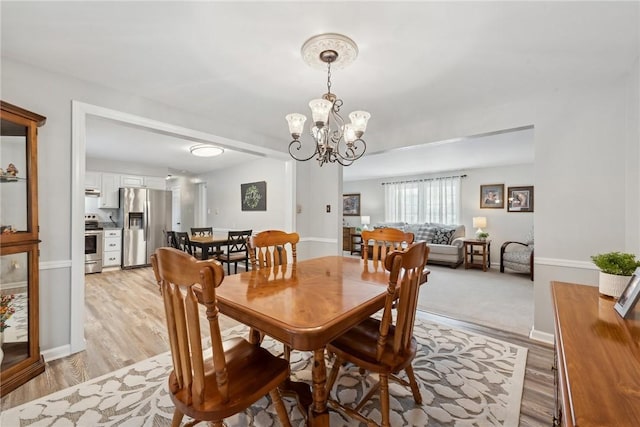 dining room featuring baseboards, light wood finished floors, and an inviting chandelier