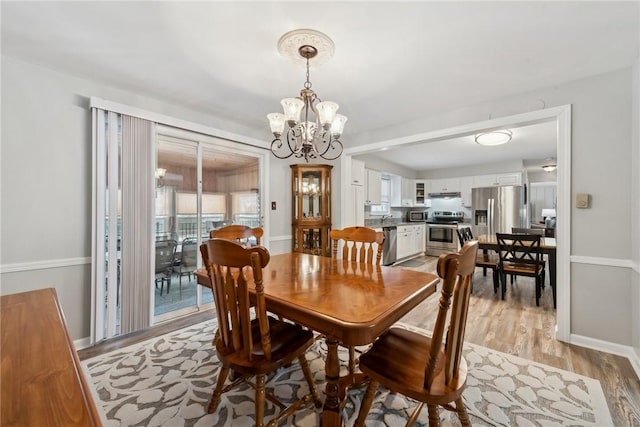 dining space with light wood-style floors, baseboards, and a notable chandelier