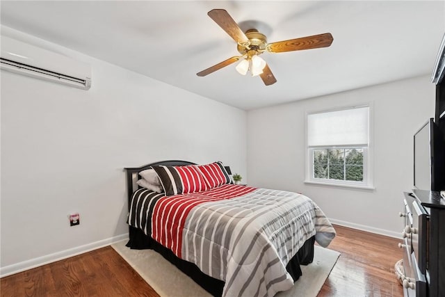 bedroom with a ceiling fan, baseboards, wood finished floors, and a wall mounted air conditioner