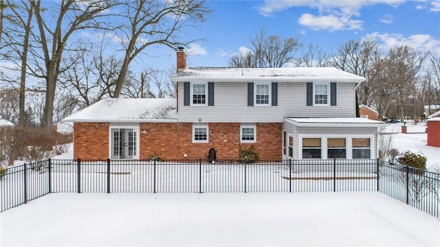 snow covered house featuring brick siding, a chimney, and fence