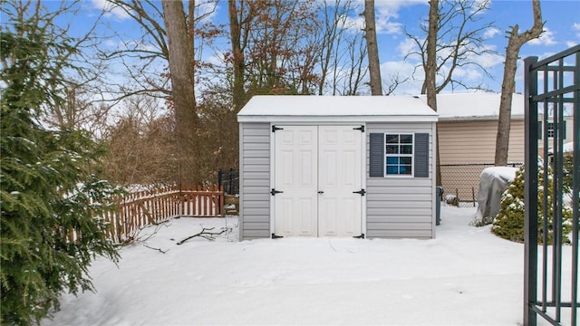 snow covered structure featuring a storage unit, an outdoor structure, and fence