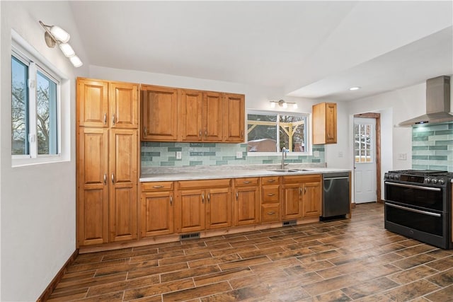 kitchen with light countertops, appliances with stainless steel finishes, a sink, plenty of natural light, and wall chimney exhaust hood