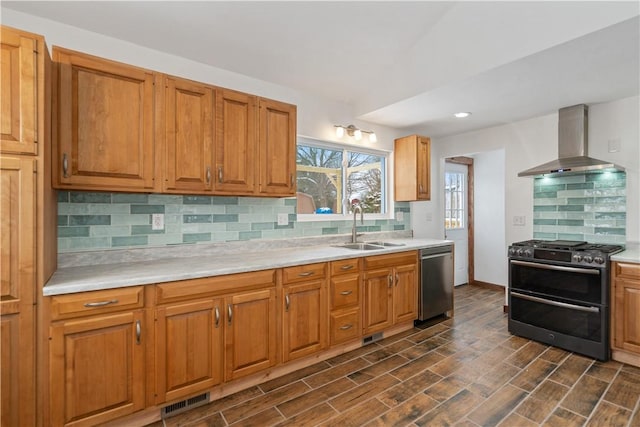 kitchen featuring stainless steel appliances, light countertops, a sink, and wall chimney range hood