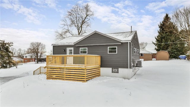 snow covered property featuring central air condition unit, a storage unit, a deck, and an outbuilding