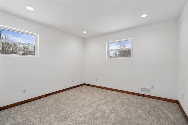 spare room featuring baseboards, light colored carpet, visible vents, and a healthy amount of sunlight