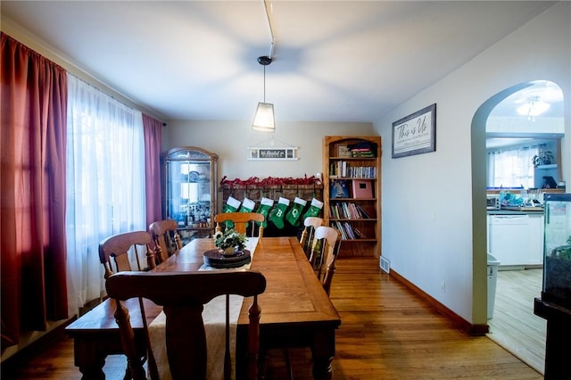 dining room with arched walkways, baseboards, and wood finished floors