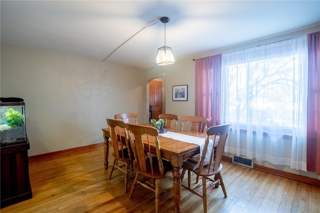 dining space featuring light wood finished floors, visible vents, arched walkways, and baseboards