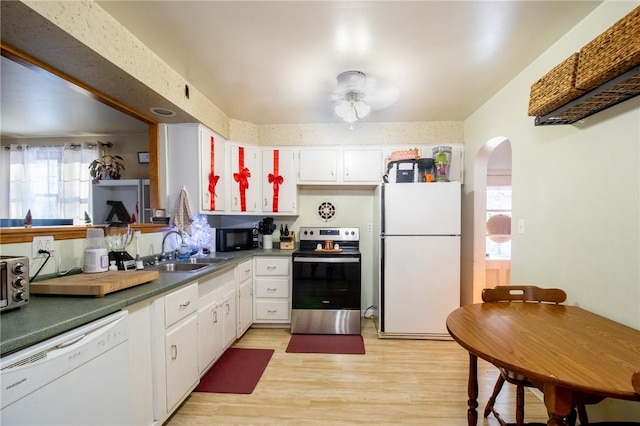 kitchen featuring arched walkways, white appliances, a sink, white cabinetry, and dark countertops