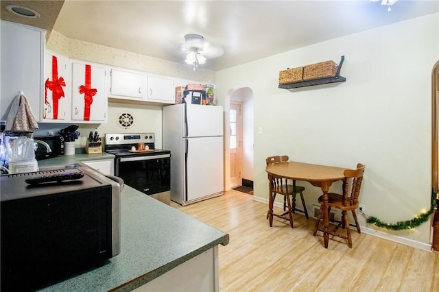 kitchen with arched walkways, freestanding refrigerator, stainless steel range with electric cooktop, white cabinets, and light wood-type flooring