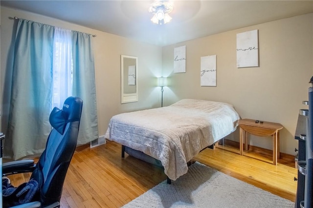 bedroom with baseboards, visible vents, and wood finished floors