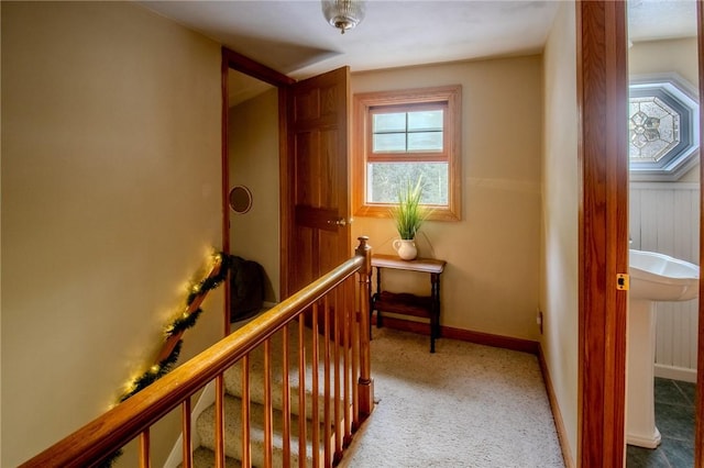 hall featuring carpet, baseboards, and an upstairs landing