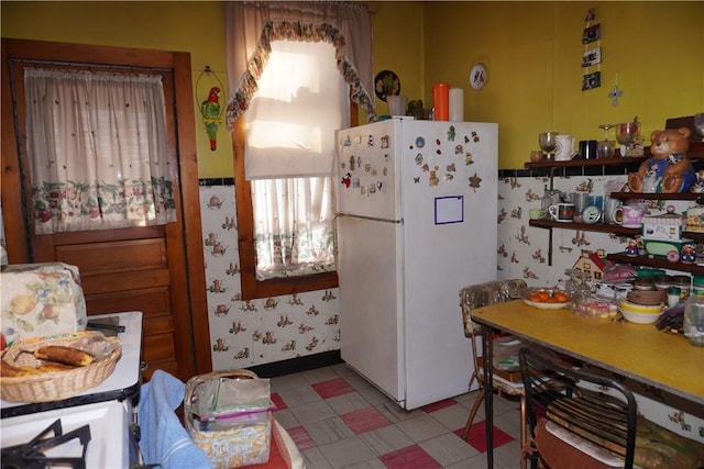 kitchen featuring freestanding refrigerator, light floors, and wallpapered walls