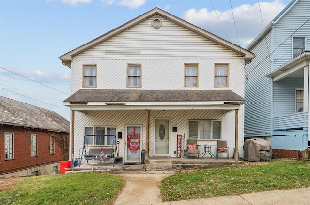 view of front of home featuring a shingled roof, covered porch, and a front lawn