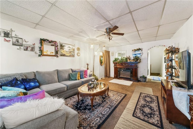 carpeted living area featuring a paneled ceiling, ceiling fan, arched walkways, and a glass covered fireplace