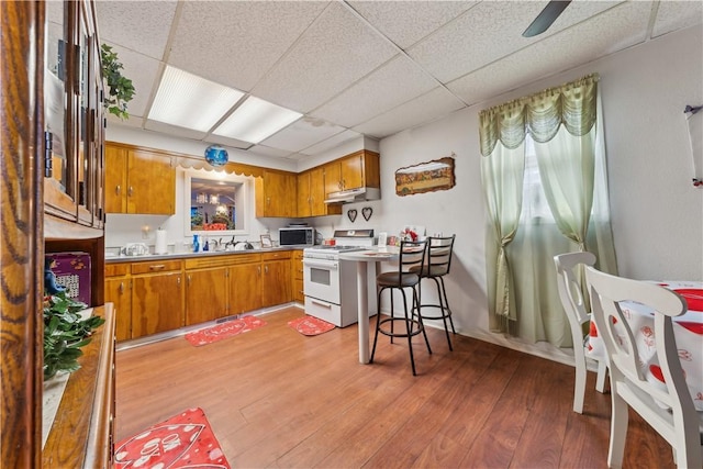 kitchen with brown cabinets, white gas stove, light wood-style flooring, a sink, and under cabinet range hood