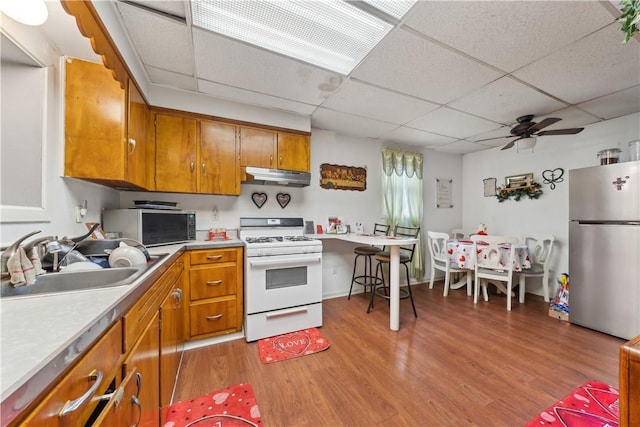 kitchen featuring under cabinet range hood, a sink, white range with gas cooktop, freestanding refrigerator, and brown cabinets