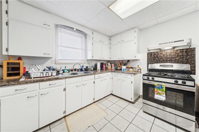 kitchen featuring white cabinets, dark countertops, under cabinet range hood, a sink, and gas stove