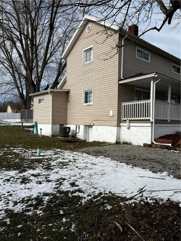 snow covered back of property featuring cooling unit and a chimney