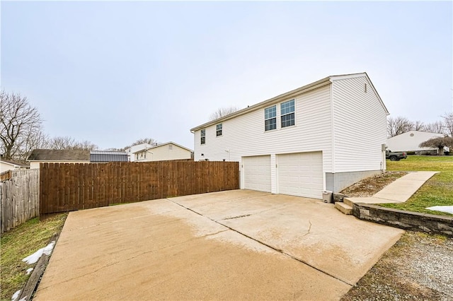 rear view of property featuring driveway, an attached garage, and fence