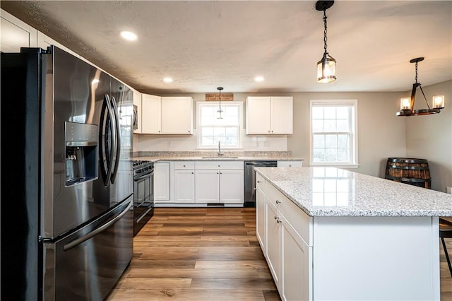 kitchen with appliances with stainless steel finishes, hanging light fixtures, light stone countertops, white cabinetry, and a sink