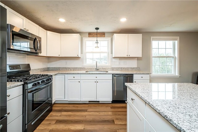 kitchen with dishwashing machine, a sink, stainless steel microwave, decorative light fixtures, and black gas range oven