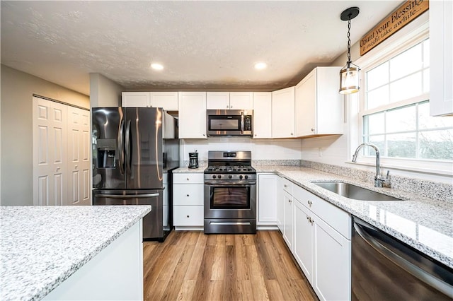 kitchen featuring white cabinets, light stone countertops, stainless steel appliances, pendant lighting, and a sink