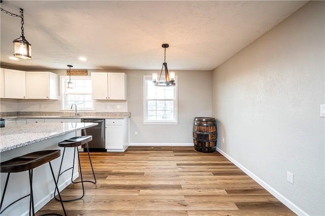 kitchen featuring white cabinetry, light stone counters, stainless steel dishwasher, and decorative light fixtures