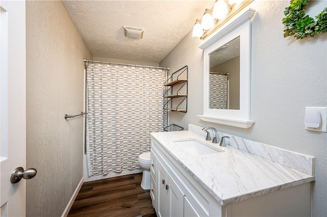 bathroom with a textured ceiling, toilet, wood finished floors, vanity, and visible vents