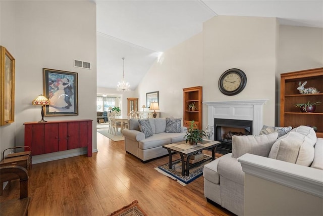 living room with high vaulted ceiling, a notable chandelier, a fireplace, wood finished floors, and visible vents