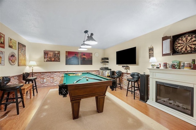 rec room with light wood-style floors, a glass covered fireplace, wainscoting, a textured ceiling, and billiards