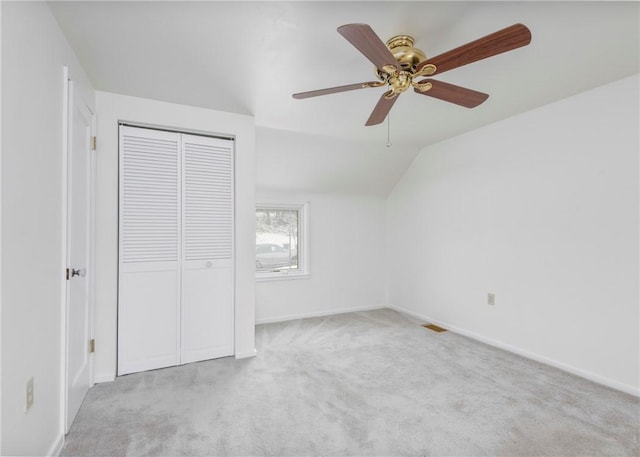 unfurnished bedroom featuring lofted ceiling, a closet, light carpet, and baseboards