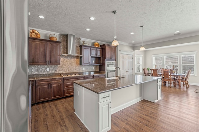 kitchen featuring a kitchen island with sink, wall chimney range hood, dark wood-style floors, and appliances with stainless steel finishes