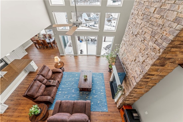 living area with a towering ceiling, a ceiling fan, and wood finished floors