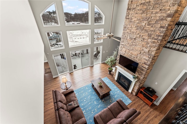 living area with a glass covered fireplace, baseboards, a high ceiling, and wood finished floors