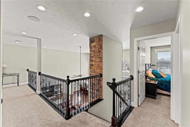 hallway with a textured ceiling, recessed lighting, light carpet, an upstairs landing, and baseboards