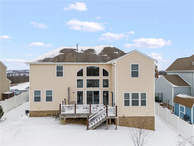 snow covered rear of property with a fenced backyard and a deck