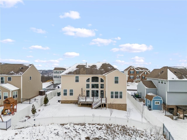 snow covered property featuring an outbuilding, a storage unit, a residential view, a fenced backyard, and a wooden deck