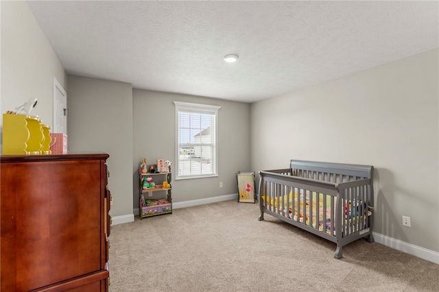 bedroom with light carpet, a nursery area, baseboards, and a textured ceiling