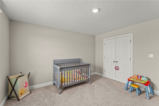 bedroom with a closet, light colored carpet, a textured ceiling, and baseboards