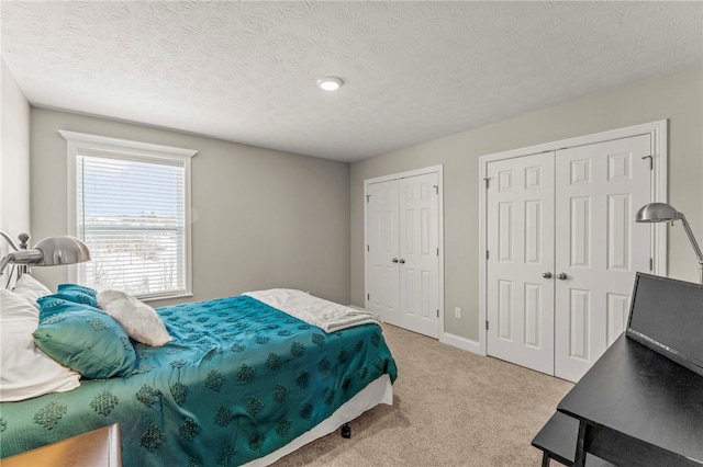 carpeted bedroom with a textured ceiling, baseboards, and multiple closets