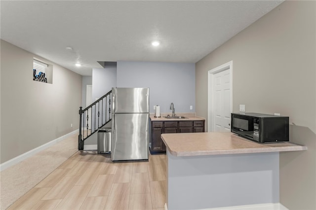 kitchen featuring light countertops, freestanding refrigerator, a sink, black microwave, and a peninsula