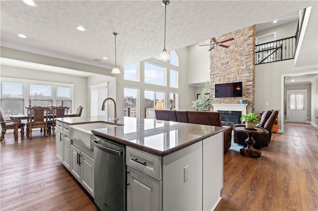 kitchen with pendant lighting, stainless steel dishwasher, open floor plan, a kitchen island with sink, and a sink