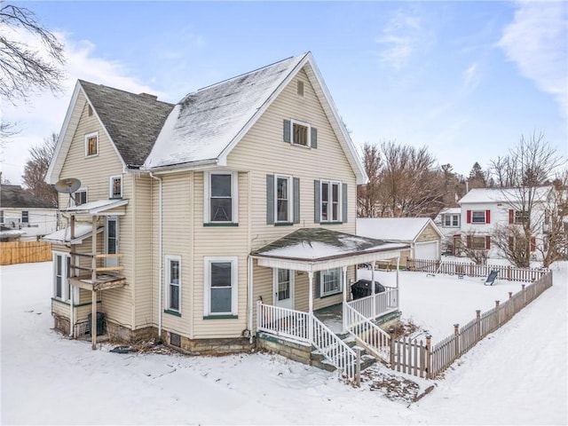 snow covered back of property featuring covered porch and fence