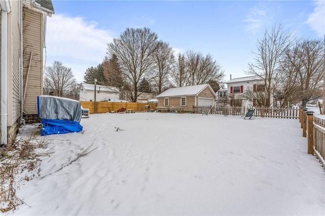 yard covered in snow with a garage, a fenced backyard, and an outdoor structure