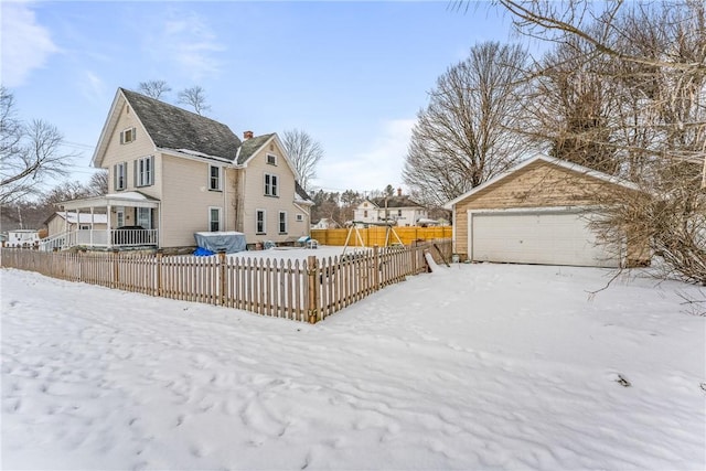 yard layered in snow with an outbuilding, a detached garage, a residential view, and fence