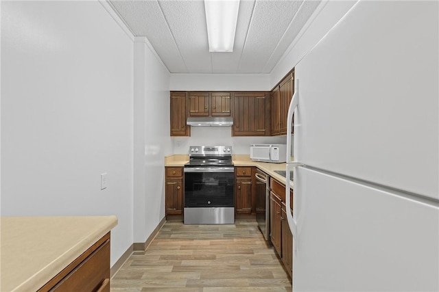 kitchen featuring a textured ceiling, under cabinet range hood, stainless steel appliances, light countertops, and light wood finished floors